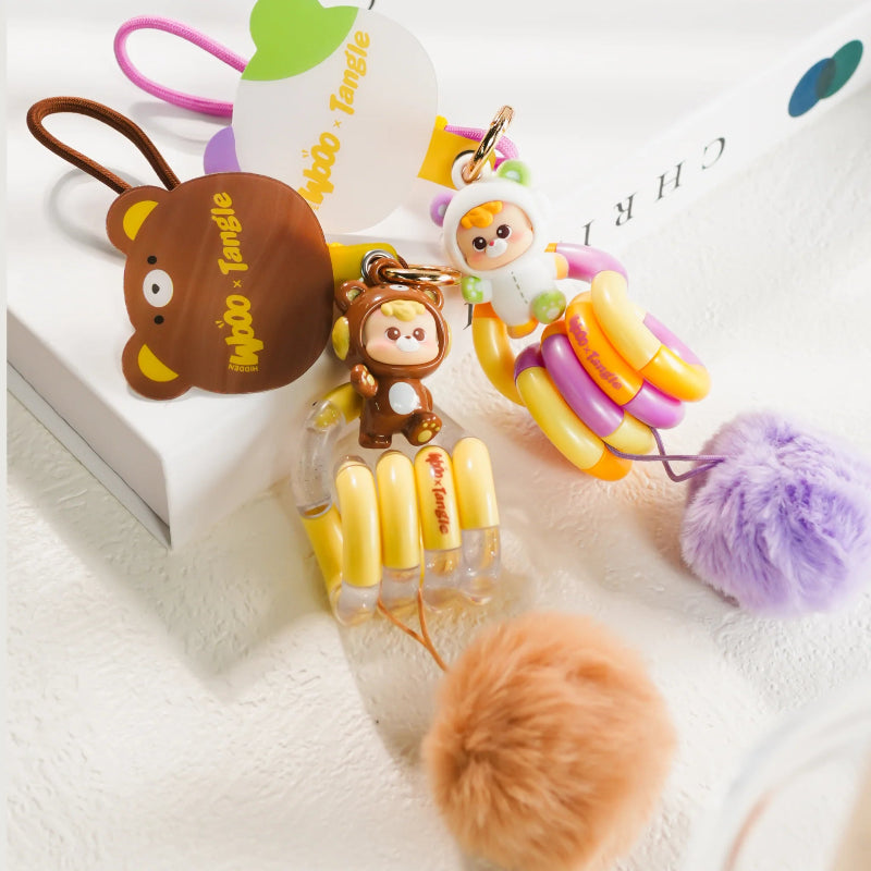 Sfeerfoto met bruine en paarse DiuDiu Baby Bear Tangle Keychain figuren uit de Tangle x HiddenWooo Blind Box collectie voor verzamelaars.