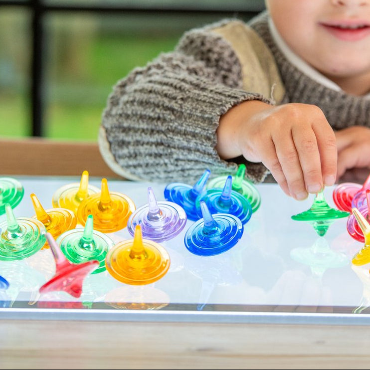 kind speelt met doorzichtige tollen van tickit op lichttafel, fijne motoriek spelgoed