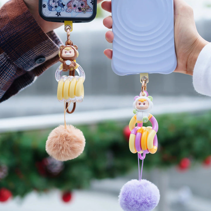 Bruine en paarse DiuDiu Baby Bear Tangle Keychain hangend aan een telefoon als schattige kawaii telefoonhanger.