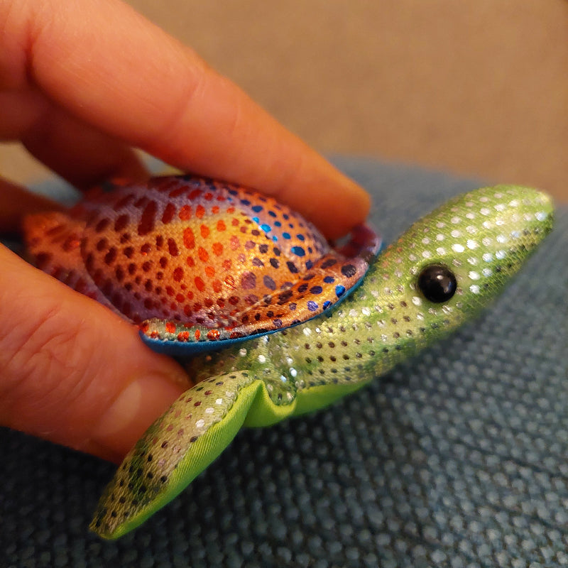 mini regenbogen schildpad groen, langnek schildpad zanddier groen met hand op blauw doek