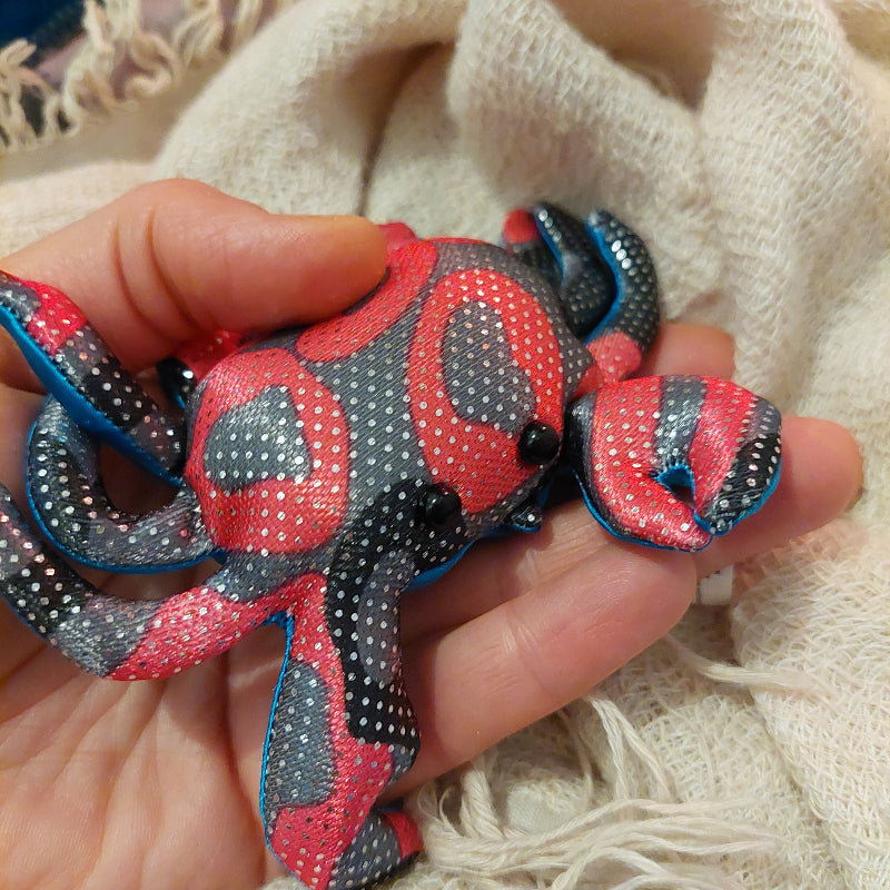 rood, zwarte kleine mini zanddier kreeft op hand, achtgrond beige deken, sensoriek speelgoed