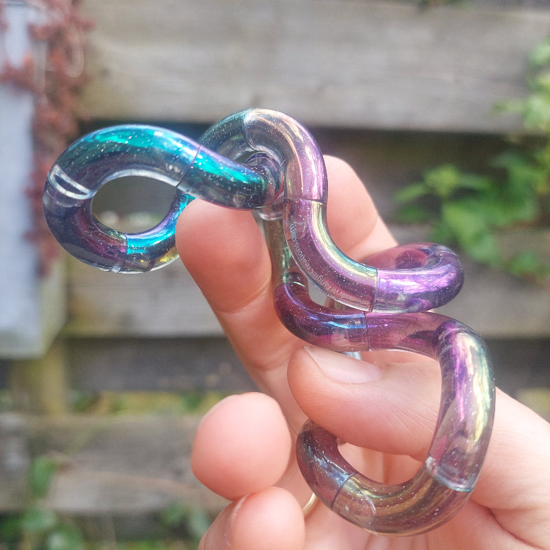 nieuwe tangle gem, zwart regenbogen transparent met olieeffect, in hand voor houten schutting, fidget tangle