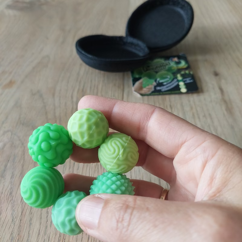 fidgnetic magneetballen, 6 magneetballen in etui, glow in the dark. Hand houd ballen, op achtergrond etui van de fidget ballen