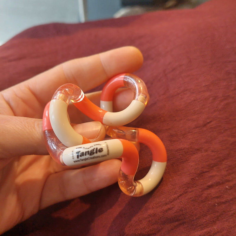 classic tangle in zachte perziek kleur, oranje, transparent en beige, in hand op bordaux kleurig achtergrond van stof, si materiaal voor autistme en adhd