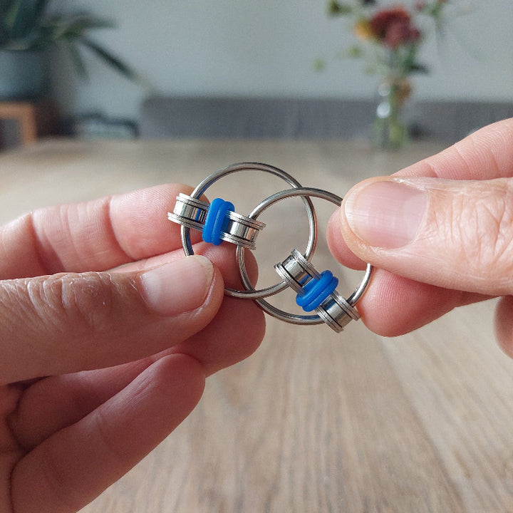 twee handen met fidget chain van metal, fidgetspeelgoed, foto aan houten tafel met bloemen op de achtergrond
