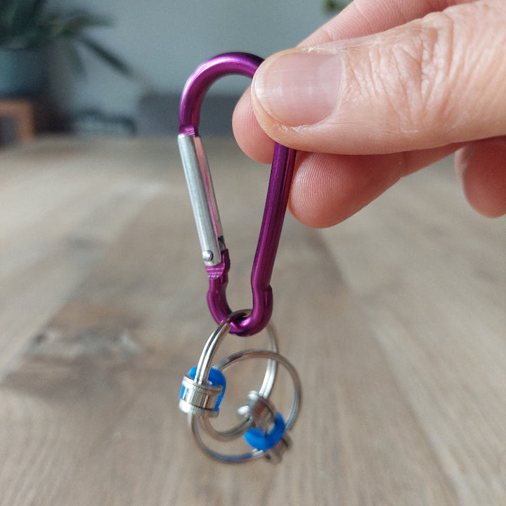 fidget chain blauw aan karabiner haak paars, fidget om mee te nemen, hand houd fidget boven houten tafel