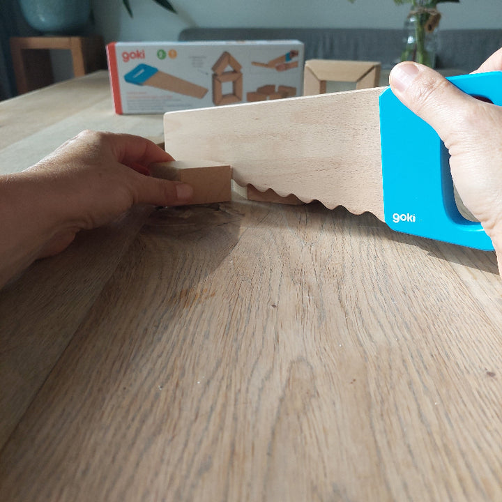 handen aan het zagen met kinderspeelgoed, houten blokken met klittenband doorzagen met een houten speelgoed zaag. motoriekspeelgoed voor bouwhoek