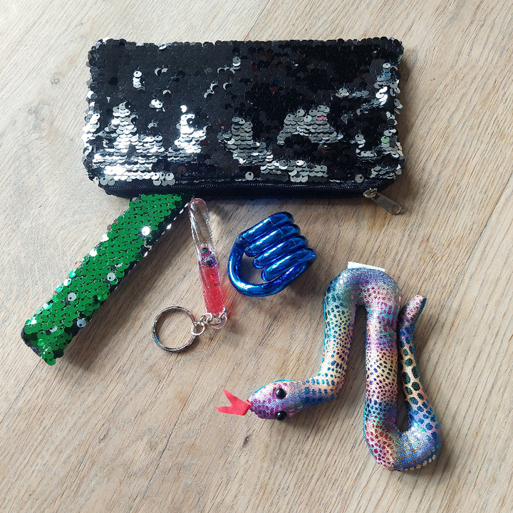 fidget etui met glitters, etui met paijetten, armband met glitter, toverstaf sleutelhanger in rood, blauwe tangle metalic look en een zanddier slang in glitter patroon, op houten tafel
