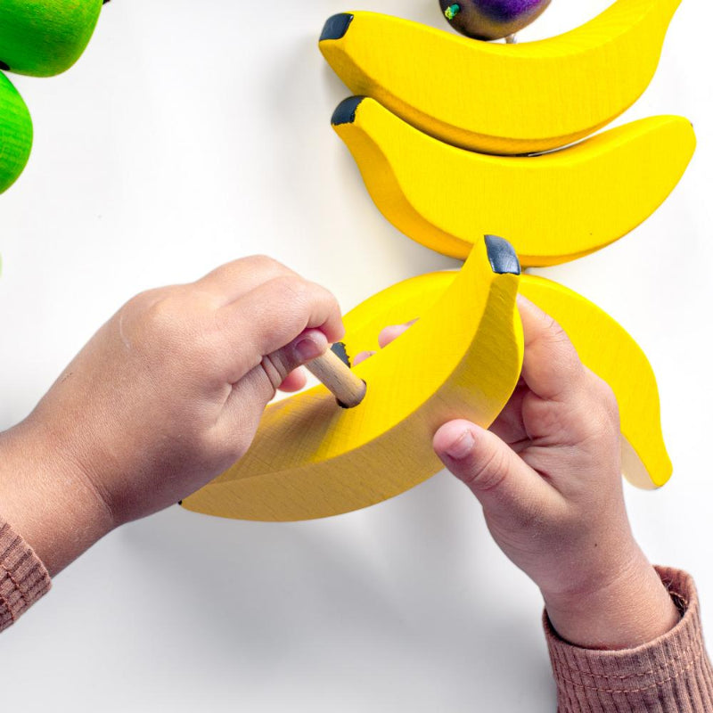 Kinderhand met rijgfruit van erzi, duurzaam speel materiaal, rijgbanaan, motoriekspeelgoed, houten speelgoed