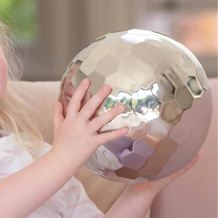 Een kind onderzoekt de glanzende sensorische tuimelbal met beide handen, tickit sensorische stalen tuimelbal, sensory play