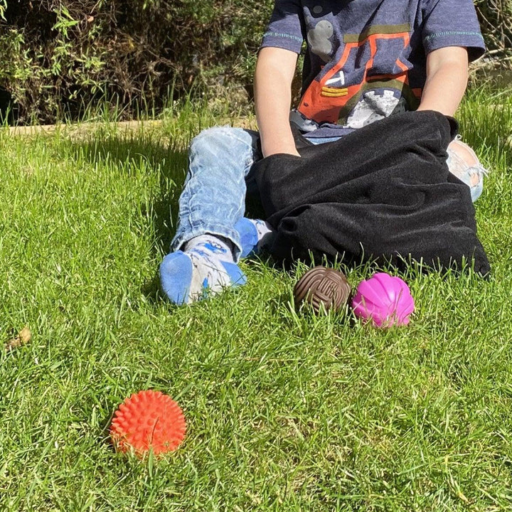 kind zit in gras met de sensoriek ballen, discovery ballen van ticket, ballen in voelzak, sensoriek spel