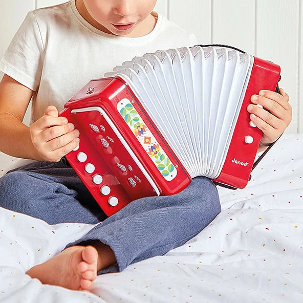 kind zit op bed en spelt met het accordeon van janod, tweehandig spelen, motoriekk speelgoed