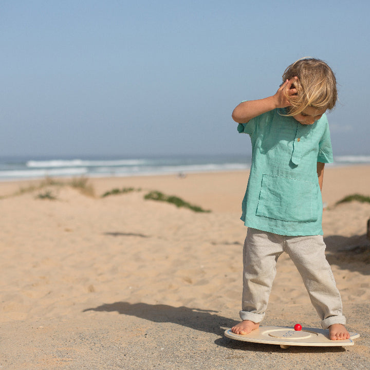 Kind oefent evenwicht op het BS Toys balanceerboard, op het strand, achtergond de zee