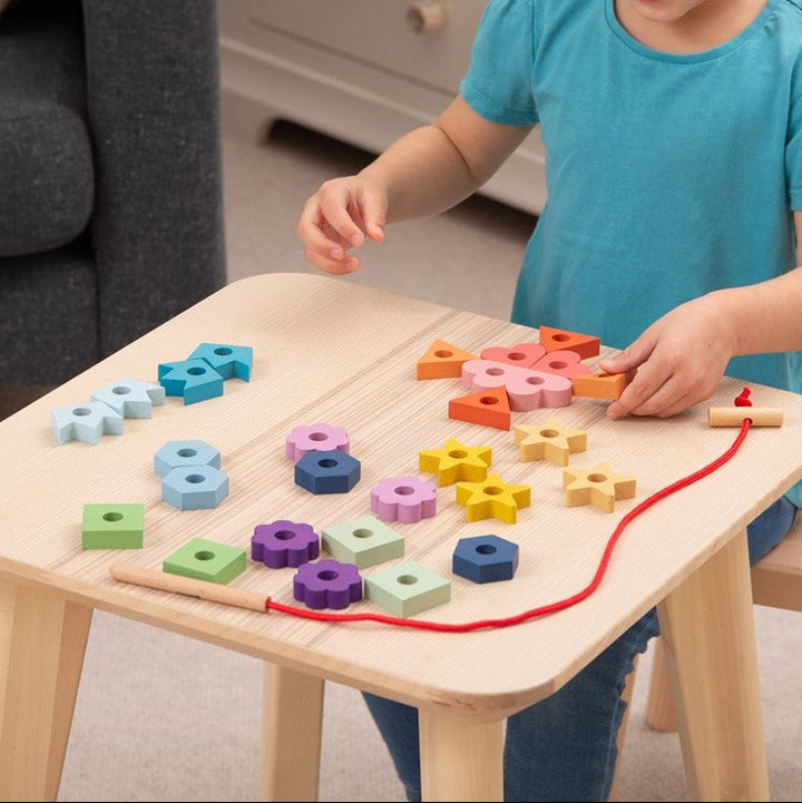 Spelend kind sorteert en rijgt houten regenboog vetervormen van Tickit, fijne motoriekspeelgoed