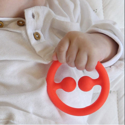 babyhand met rode sensorische bijtring van  moluk, motoriekspeelgoed voor babys