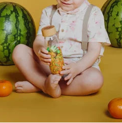 kind hout sensoriek  fles van petit boum in de hand, fles heeft fruit als inhoud, achtergondmelonen, voorgrond appels
